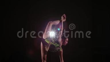 穿着色彩鲜艳的泳衣的可爱女孩运动员在黑暗的健身房里表演<strong>艺术体操</strong>元素